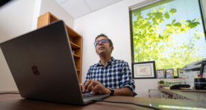 Abbas Attarwala, who was awarded a $30,000 grant this summer to research the impacts of AI on children, is photographed at his desk while he is typing on a laptop.